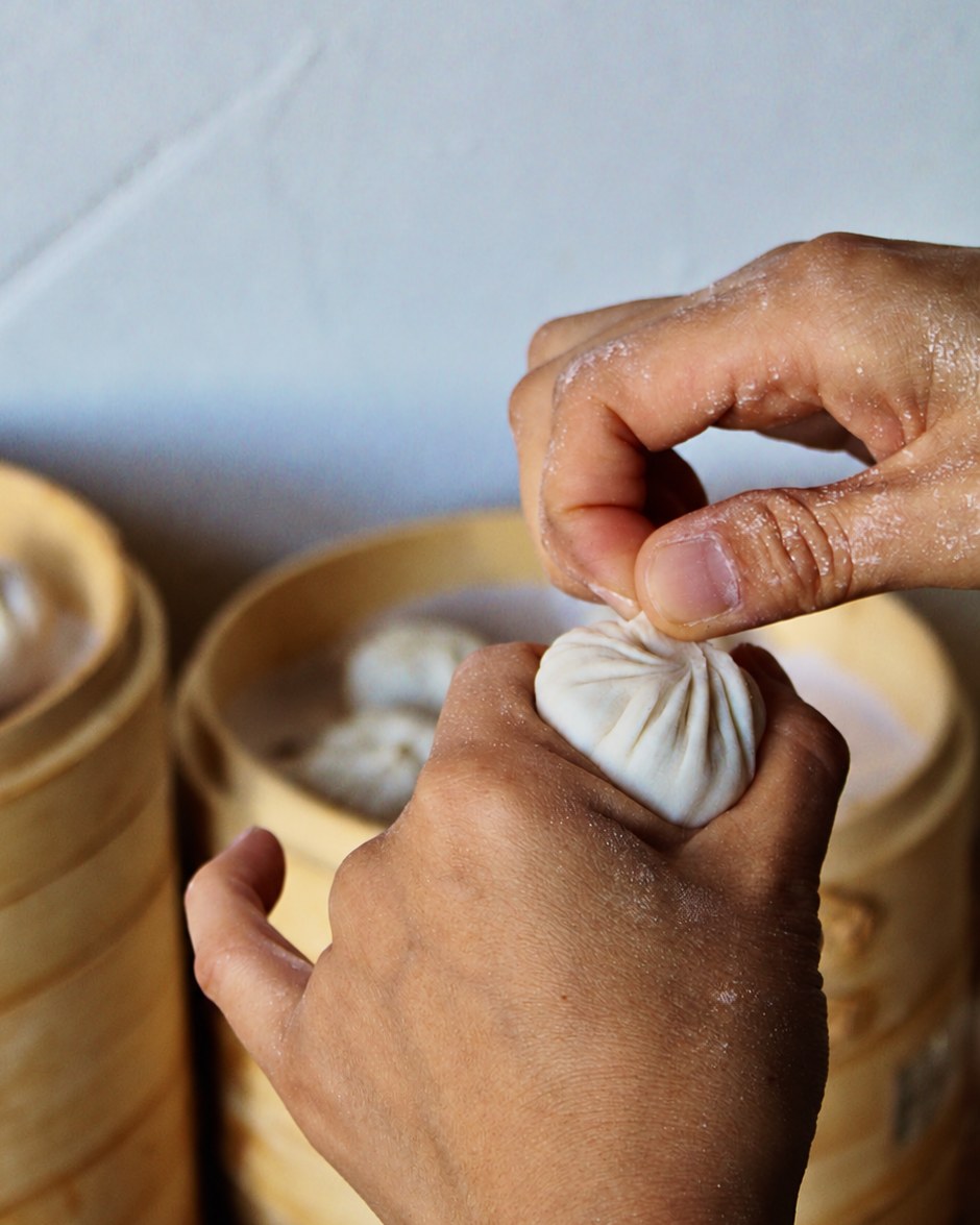Handen die een soepdumpling plooien naast bamboe stoommandjes